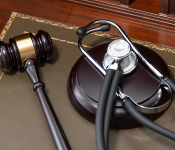 A wooden judge's gavel and a medical stethoscope resting on a green leather legal desk mat