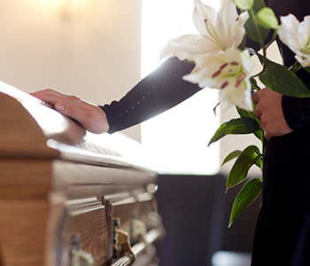 Person mourning at a casket with lilies, representing wrongful death legal services